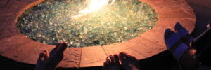 picture of fire glass pebbles burning inside of a fire pit with peoples feet on the edge